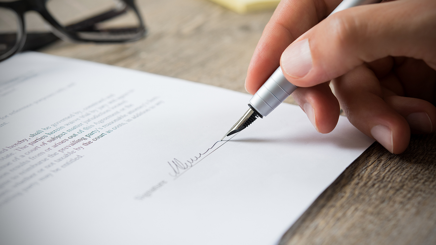 Bild på del av hand och penna som signerar ett dokument. 